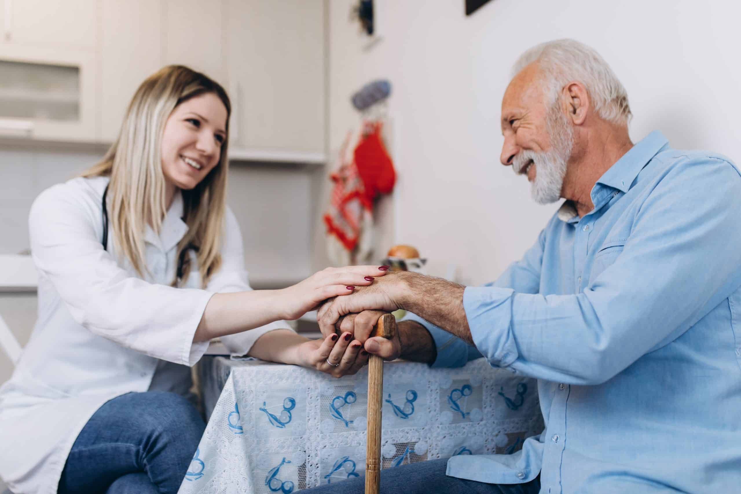 Young positive caregiver taking care of senior man in nursing home