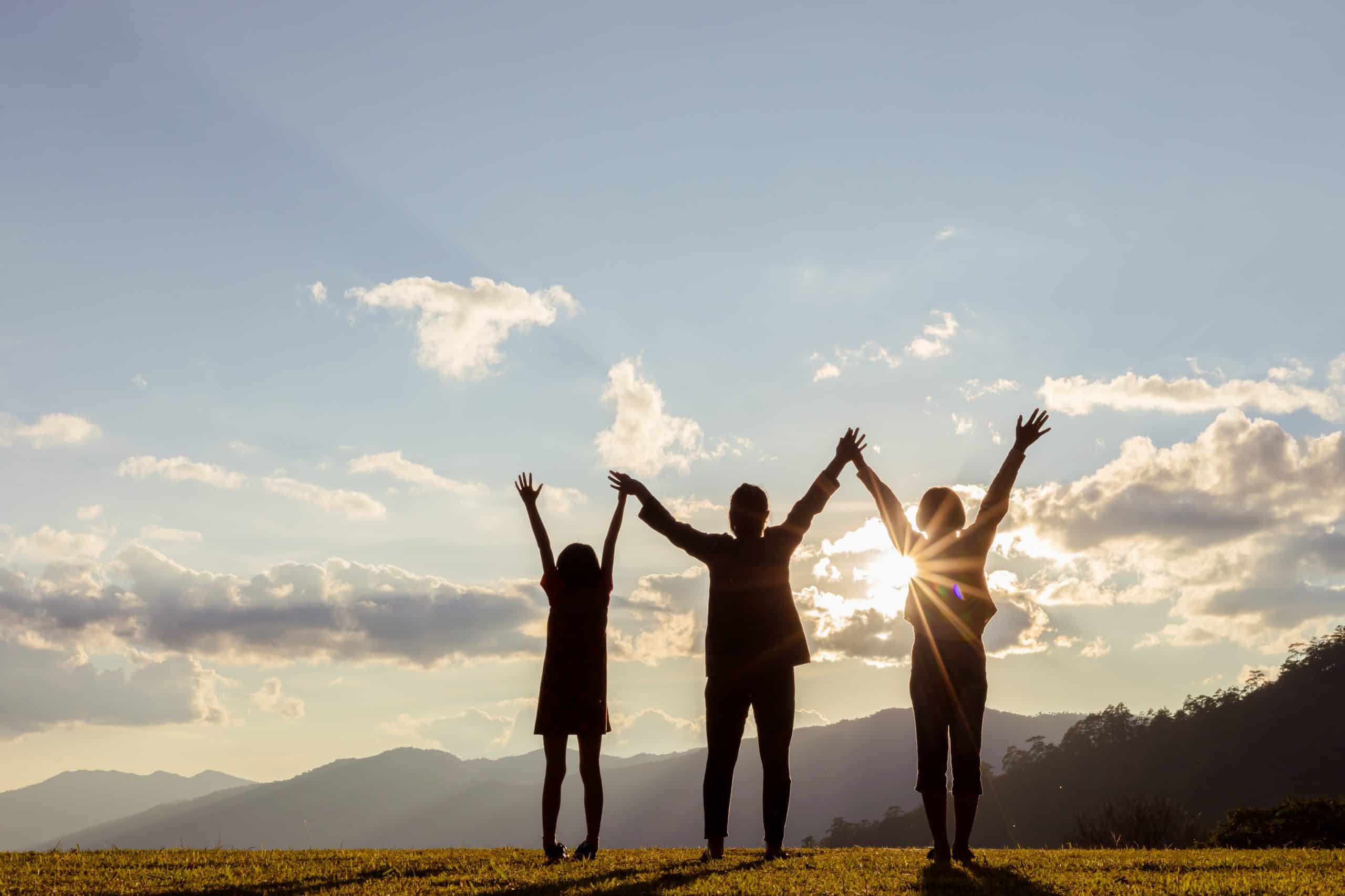 silhouette of people group with raised hands on the mountain at the sunset time.