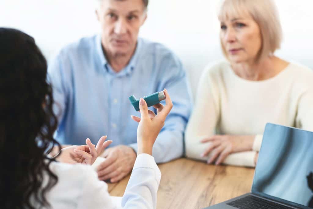 Physician giving asthma inhaler to elderly couple